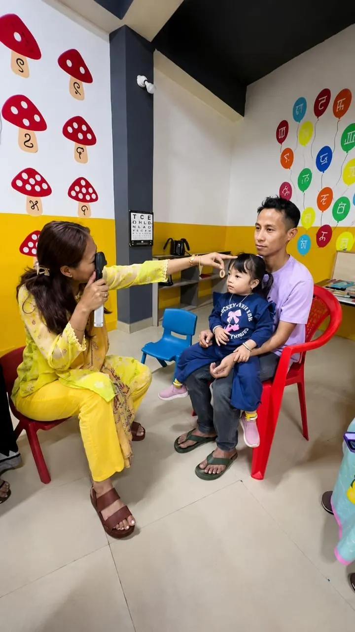 An optometrist gently examining a toddler sitting on her father's lap in the children's room