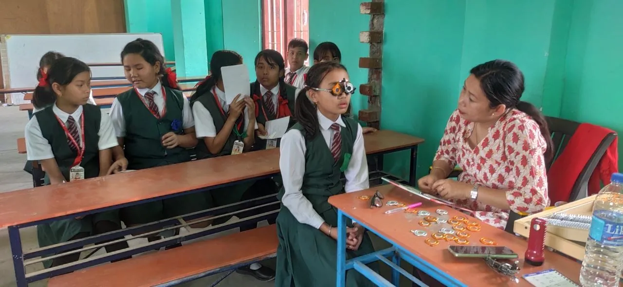 An optometrist checking a student's vision with a trial frame and lens set at a school workshop